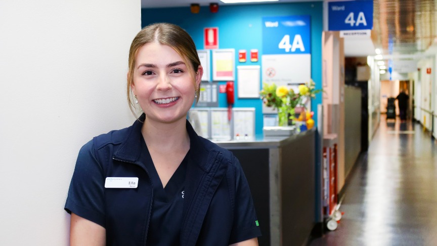 A nurse named Ella Boatfield is positioned in a hallway, wearing a blue shirt, exemplifying professionalism in healthcare
