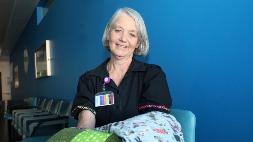 Nurse Angela Lane sits in a hospital chair, holding a blanket, symbolising her role in patient comfort and support
