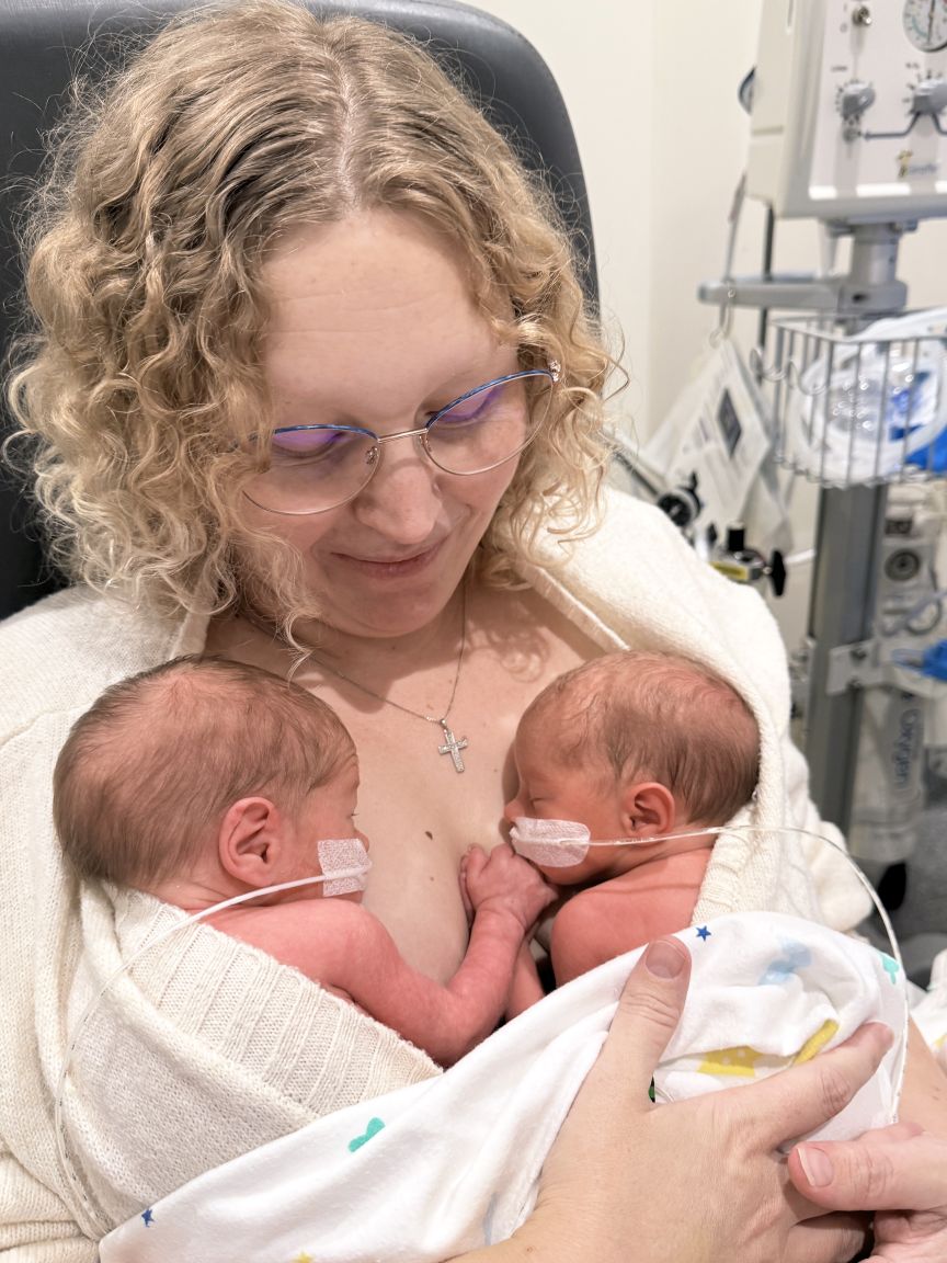 Curly haired woman holding two twins on her chest