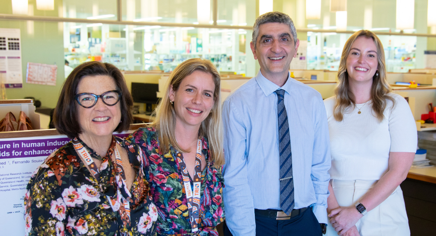Four people stand in an office, with a research poster visible in the background.