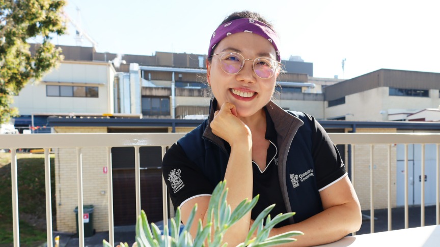 woman sitting at outdoor table in QEII uniform, smiling