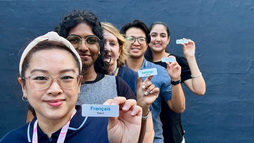 A diverse group of clinicians and students standing in a staggered line proudly displaying their language identification badges
