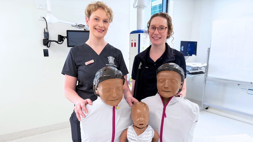 Two nurses standing behind dark skinned mannikins on a hospital bed