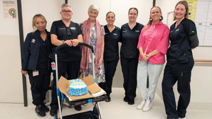 Group of people standing with a green trolley that is holding a cake
