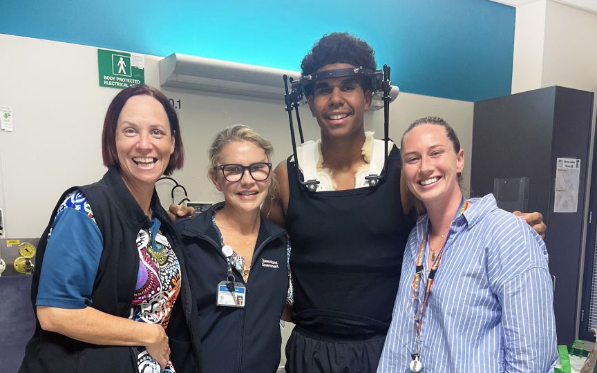 Four people, including patient Jarlii in a halo, stand together in a hospital room